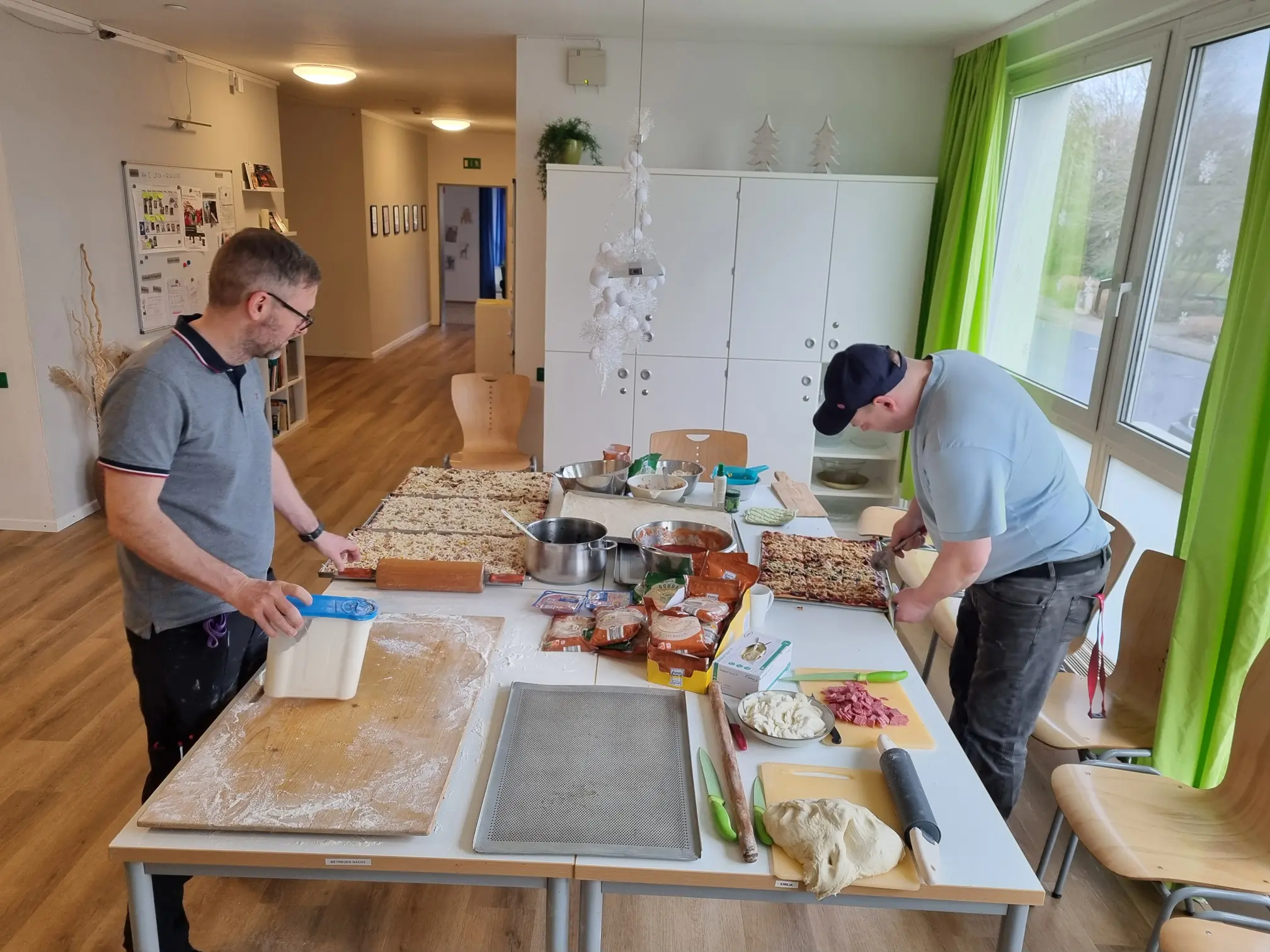 Bund der Caritasstiftungen im Bistum Hildesheim BdC, zwei Männer bereit auf einem großen Tisch Pizza vor